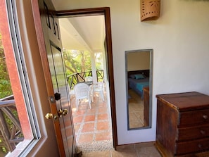 Una puerta abierta que da a un balcón con una mesa y sillas, un aparador de madera y un espejo en la pared.