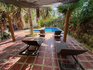 Un área junto a la piscina con sillas de descanso y suelo de baldosas.