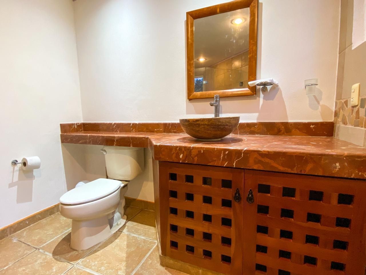 Een badkamer met een toilet, een wastafel met een marmeren aanrechtblad en een houten kast.