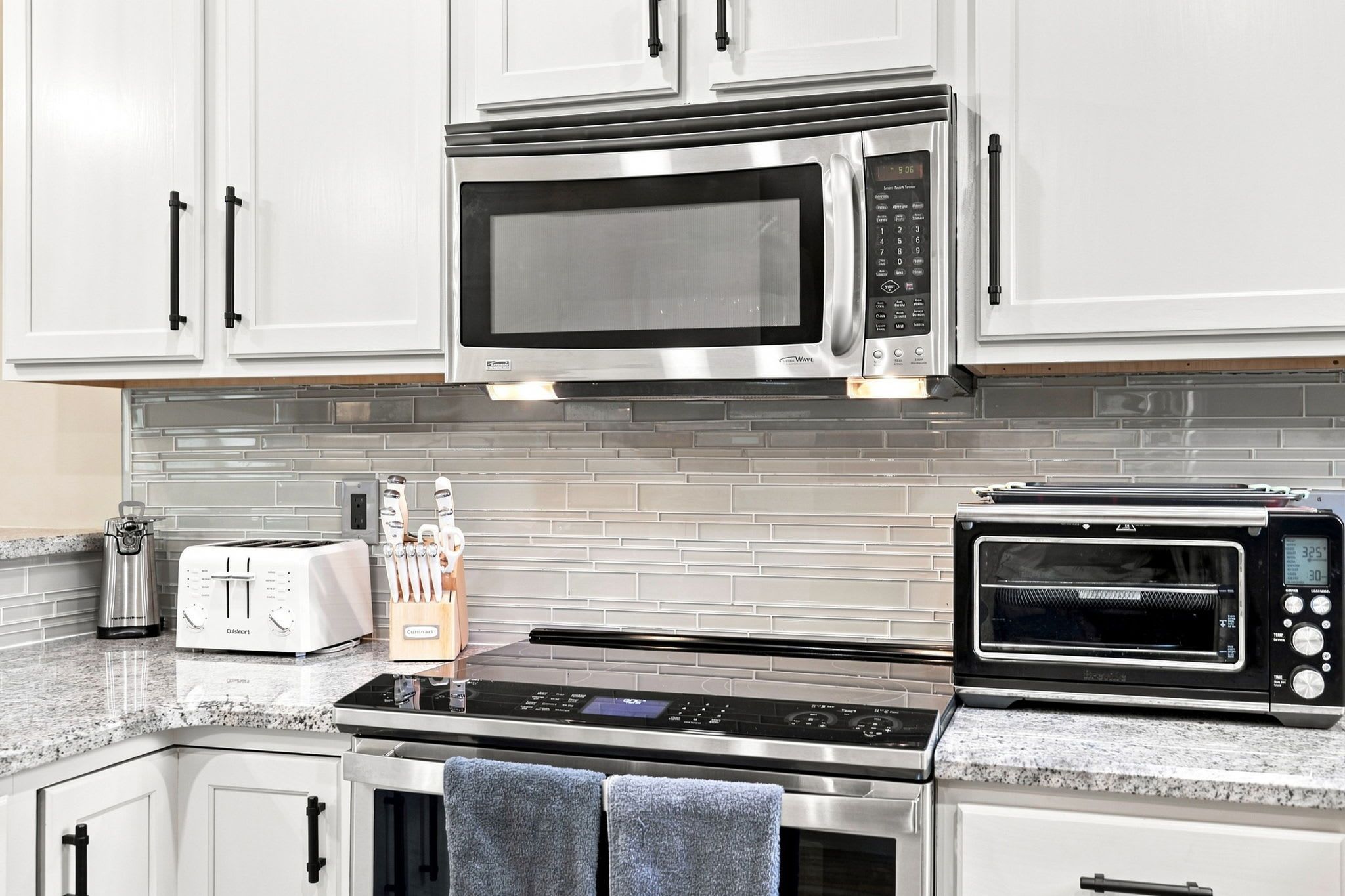 A kitchen with white cabinets, a stainless steel microwave, a toaster, and a toaster oven.