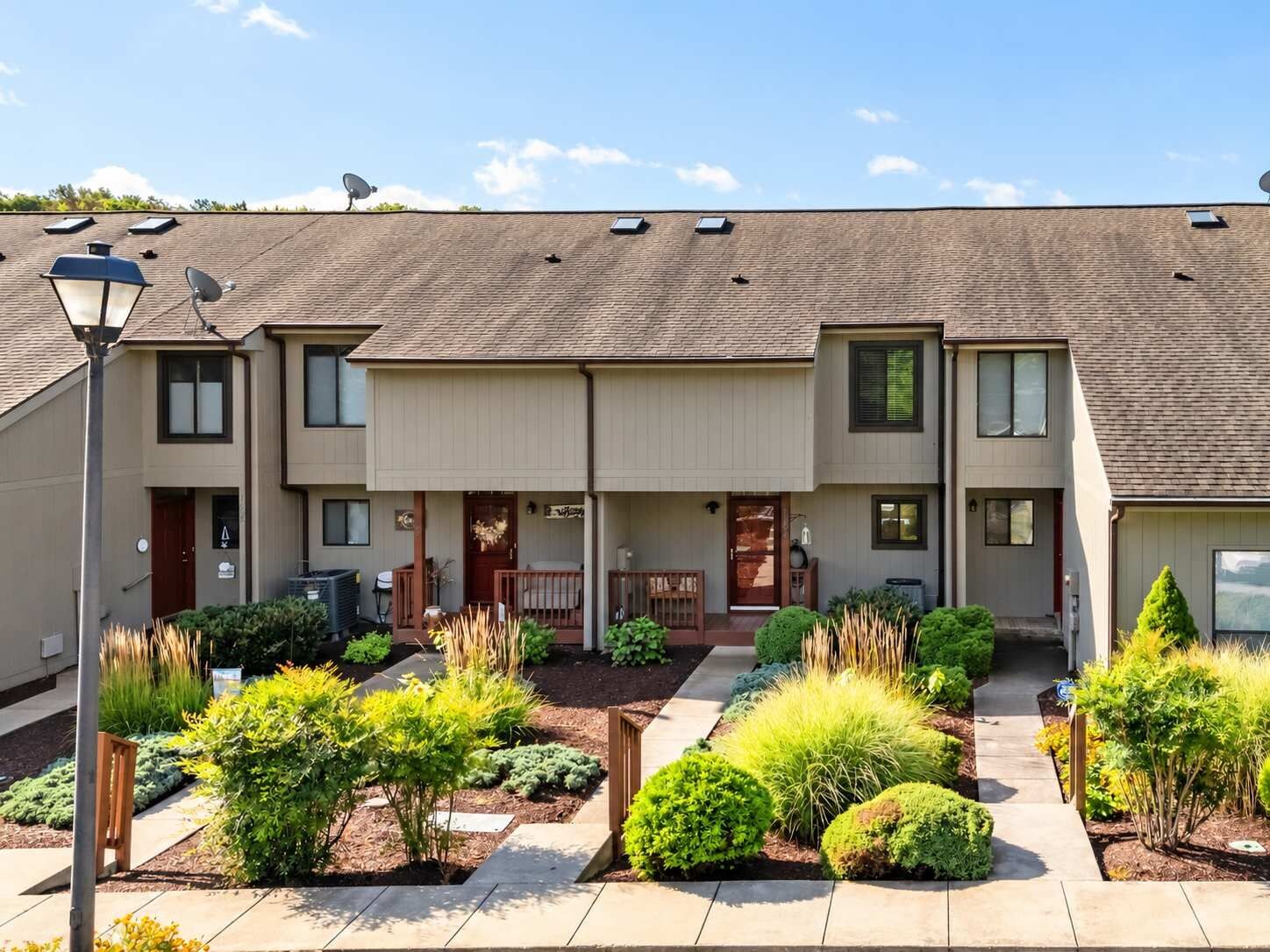 A two-story residential building with a covered patio area, satellite dishes, and a well-maintained garden with various shrubs and plants.