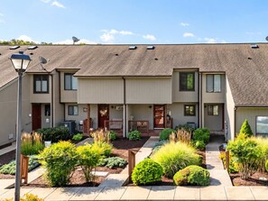 A two-story residential building with a covered patio area, satellite dishes, and a well-maintained garden with various shrubs and plants. - Lakefront w/ Resort Amenities, Multi Decks & Dogs (Hedgesville)