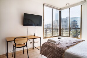 A hotel room with a bed, a desk, a chair, a television, and a large window offering a city view. - Chic Providencia Apt for 5  (Providencia)