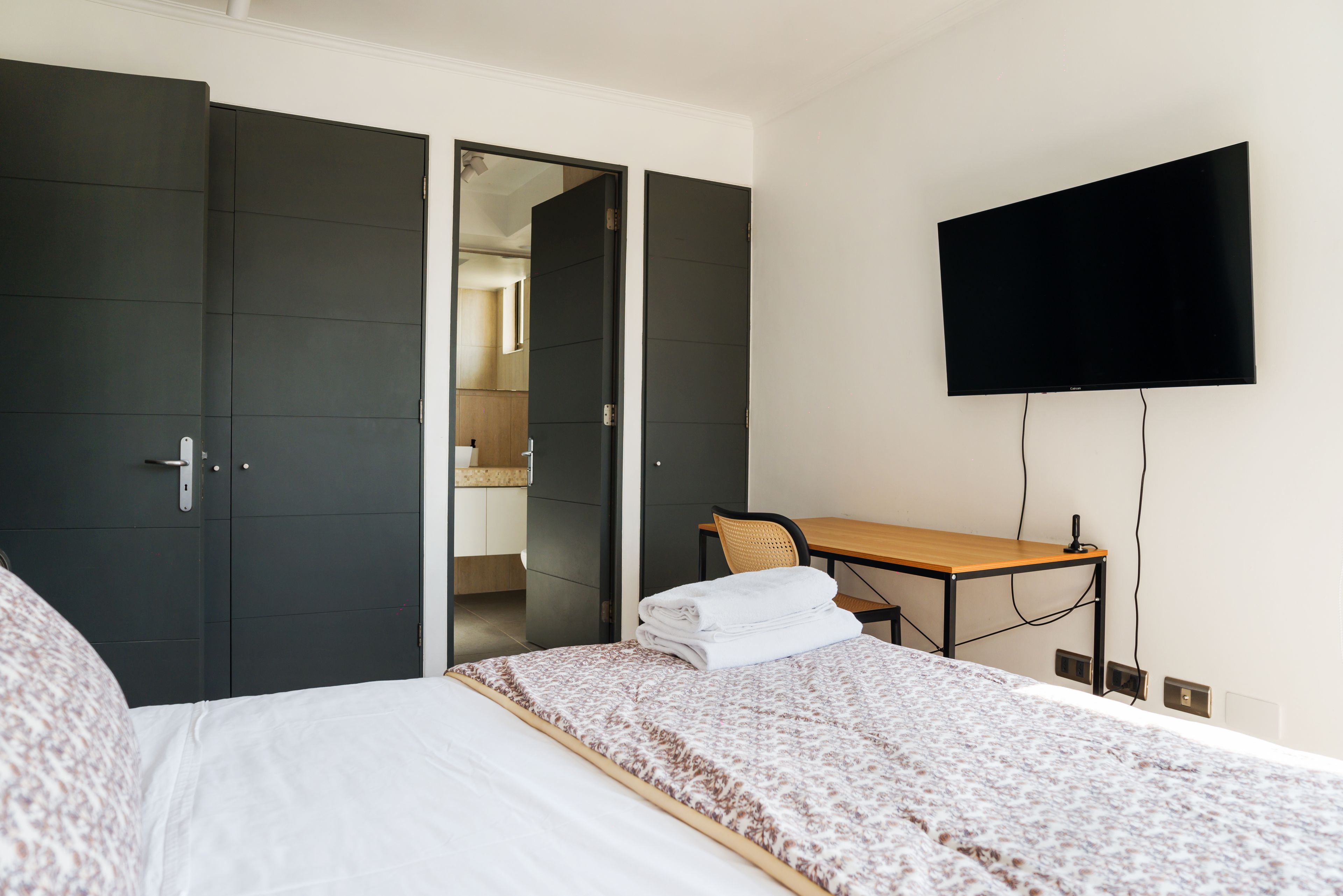 A hotel room with a bed, a desk, a flat-screen TV, and a wardrobe.
