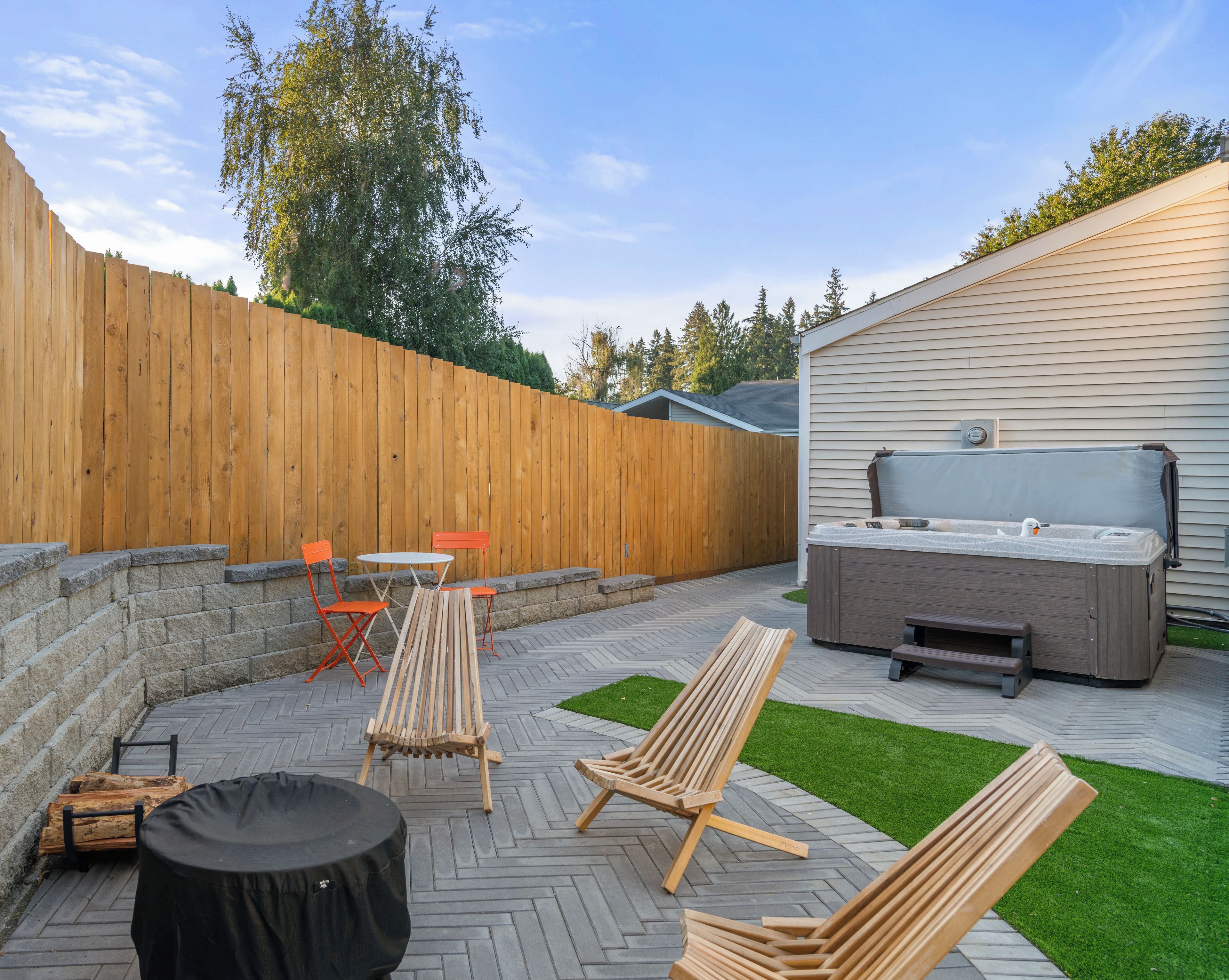 A backyard with a wooden fence, outdoor furniture, a hot tub, and a patio area.