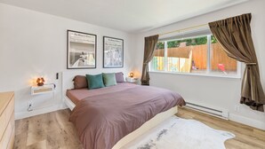 A bedroom with a large bed, two nightstands, a window with curtains, and two framed pictures on the wall. - Perfectly located Home, Spa + Mini golf - Villa 2 (Ridgefield)