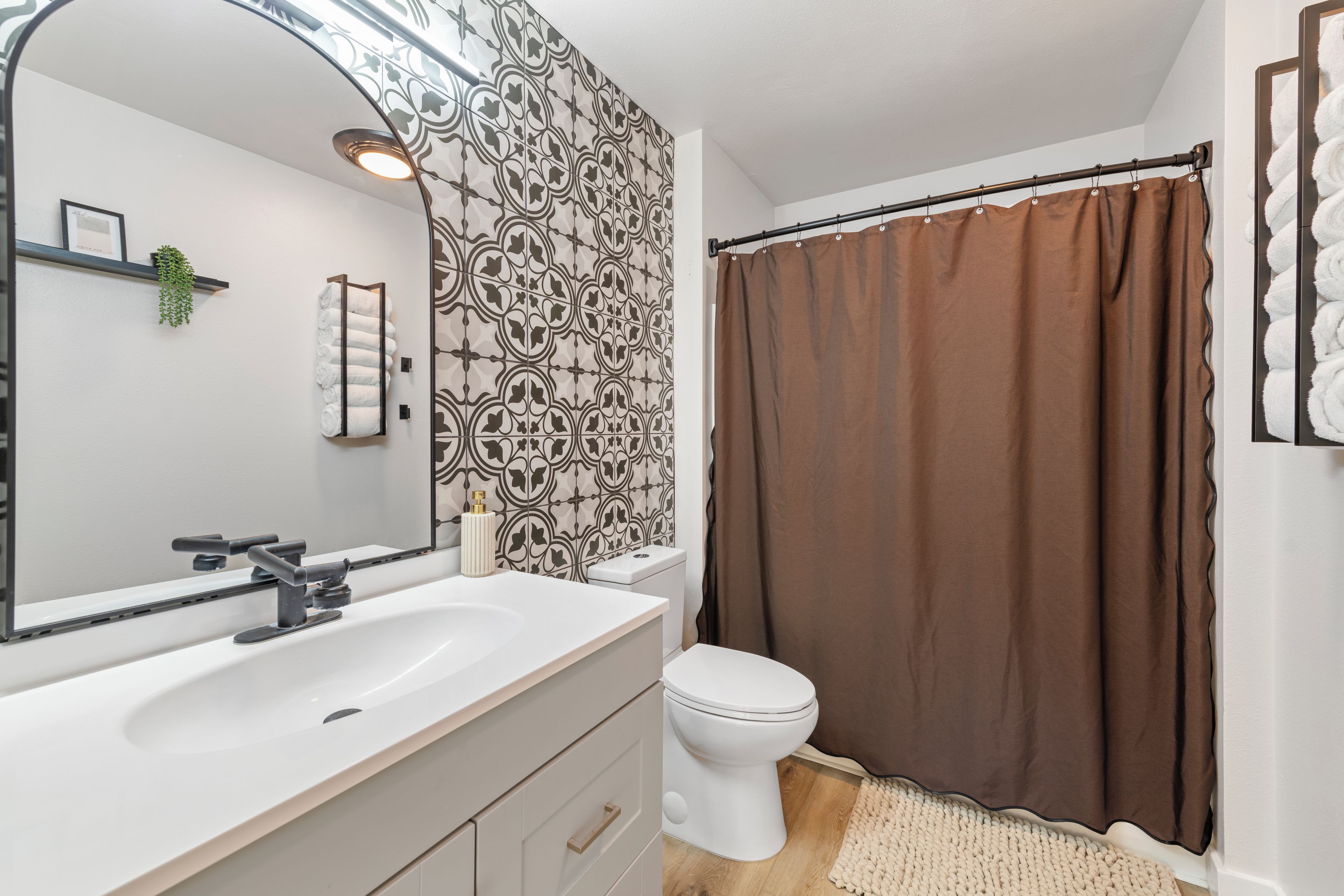 A bathroom with a white sink, a toilet, a shower curtain, and a patterned wall.