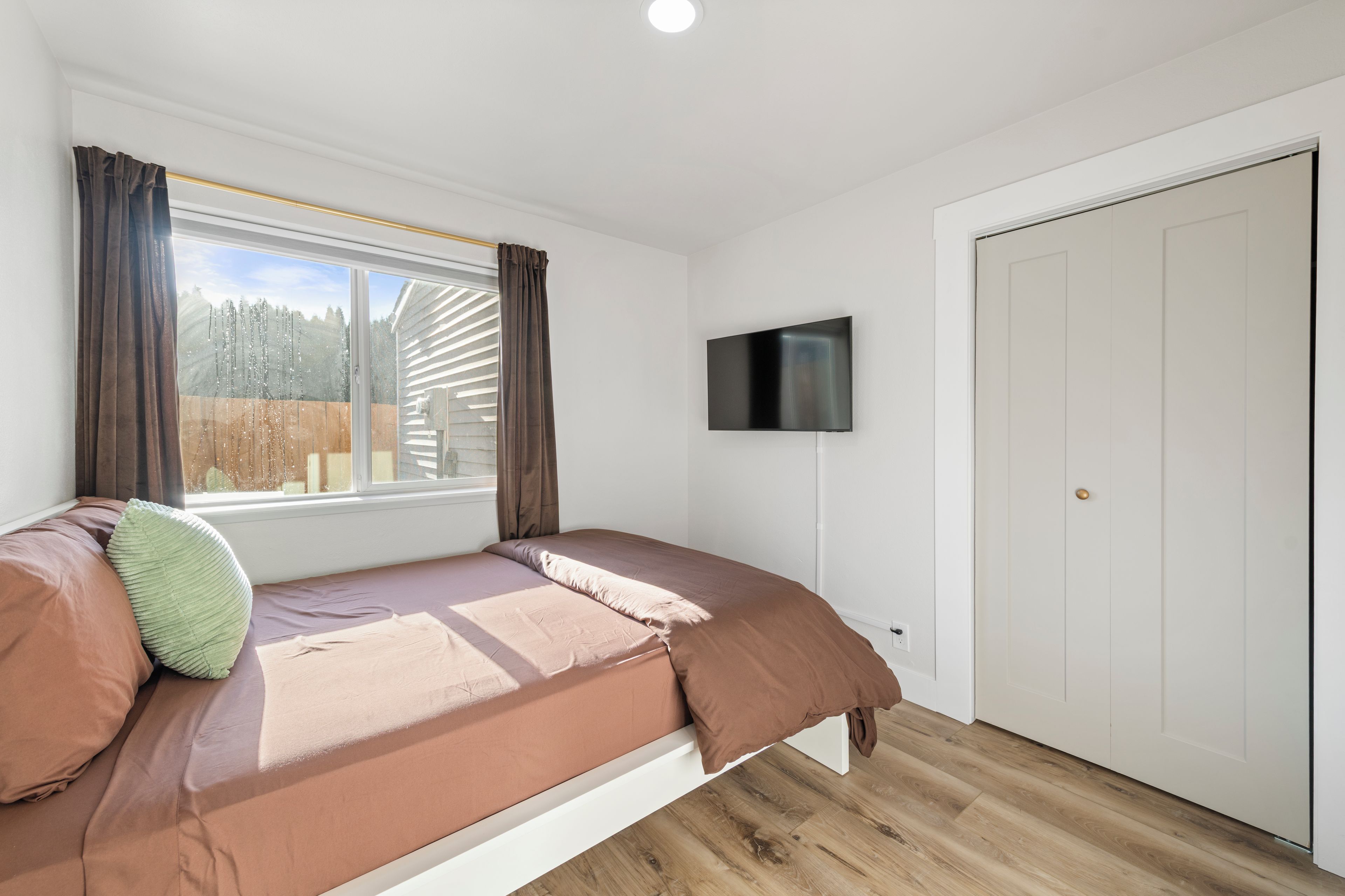 Quarto com cama, televisão, janela com cortinas e porta.