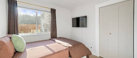 A bedroom with a bed, a TV, a window with curtains, and a door.