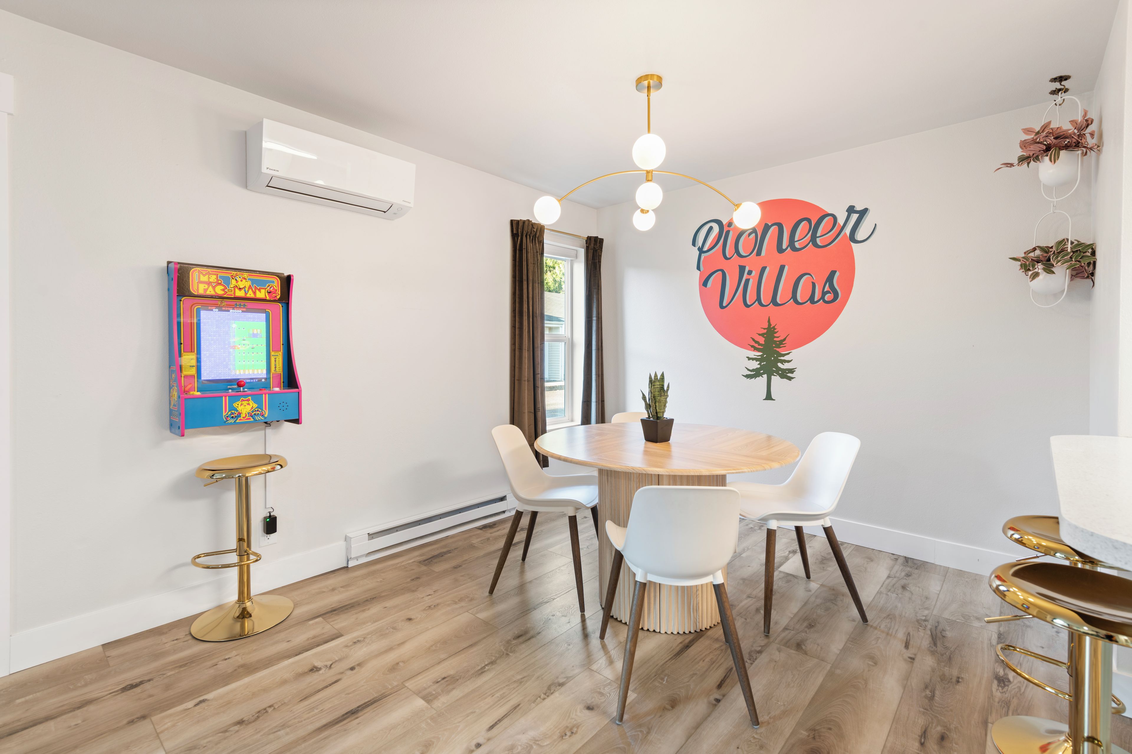 Een moderne kamer met een eettafel, stoelen, een wandairconditioner, een retro speelautomaat en een muursticker.
