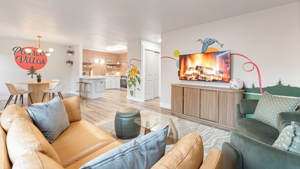 A modern living room with a sofa, a TV mounted on the wall, and a kitchen in the background. - Perfectly located Home, Spa + Mini golf - Villa 2 (Ridgefield)