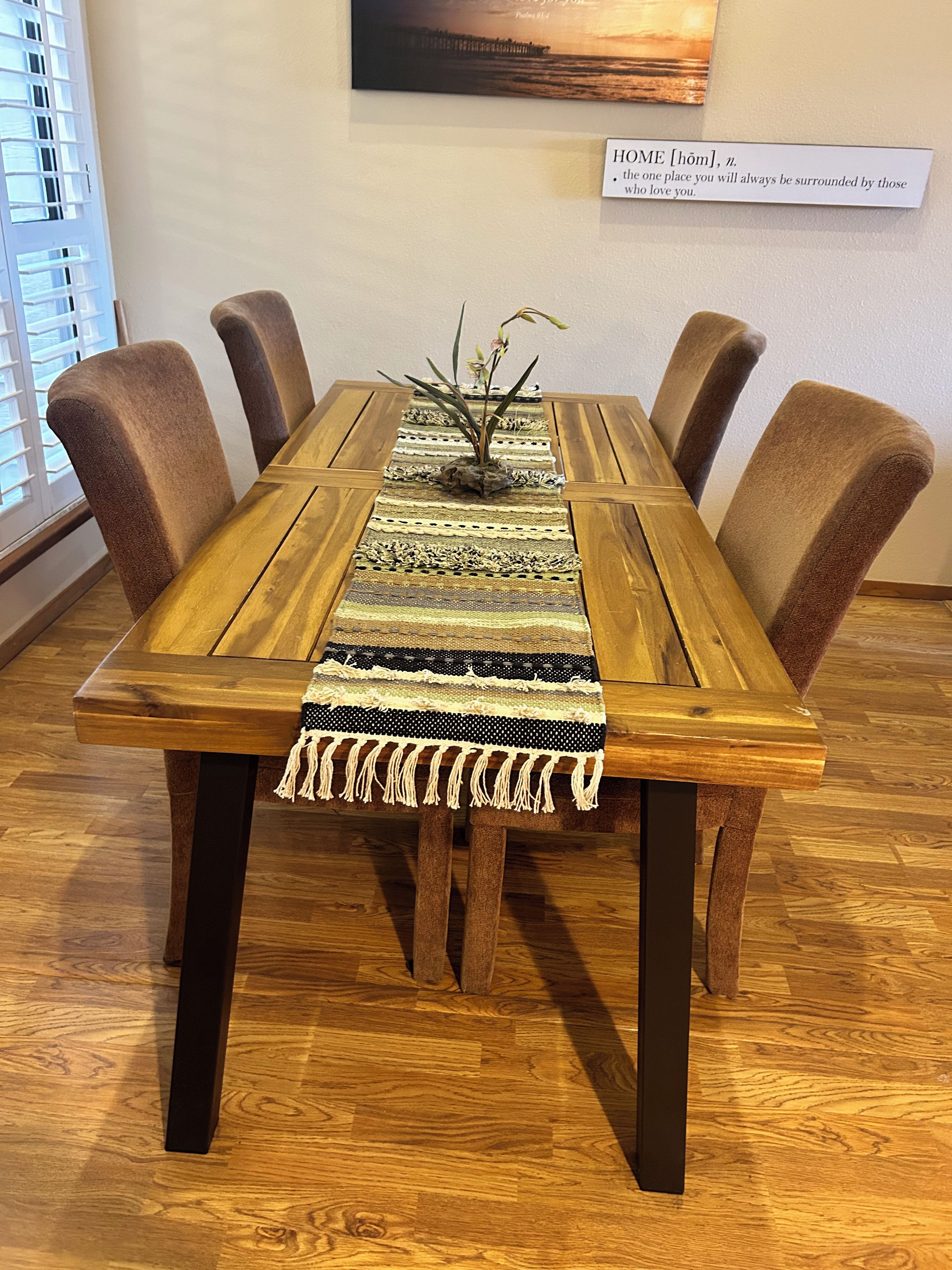 A wooden dining table with a woven placemat and a small plant centerpiece, surrounded by upholstered chairs.