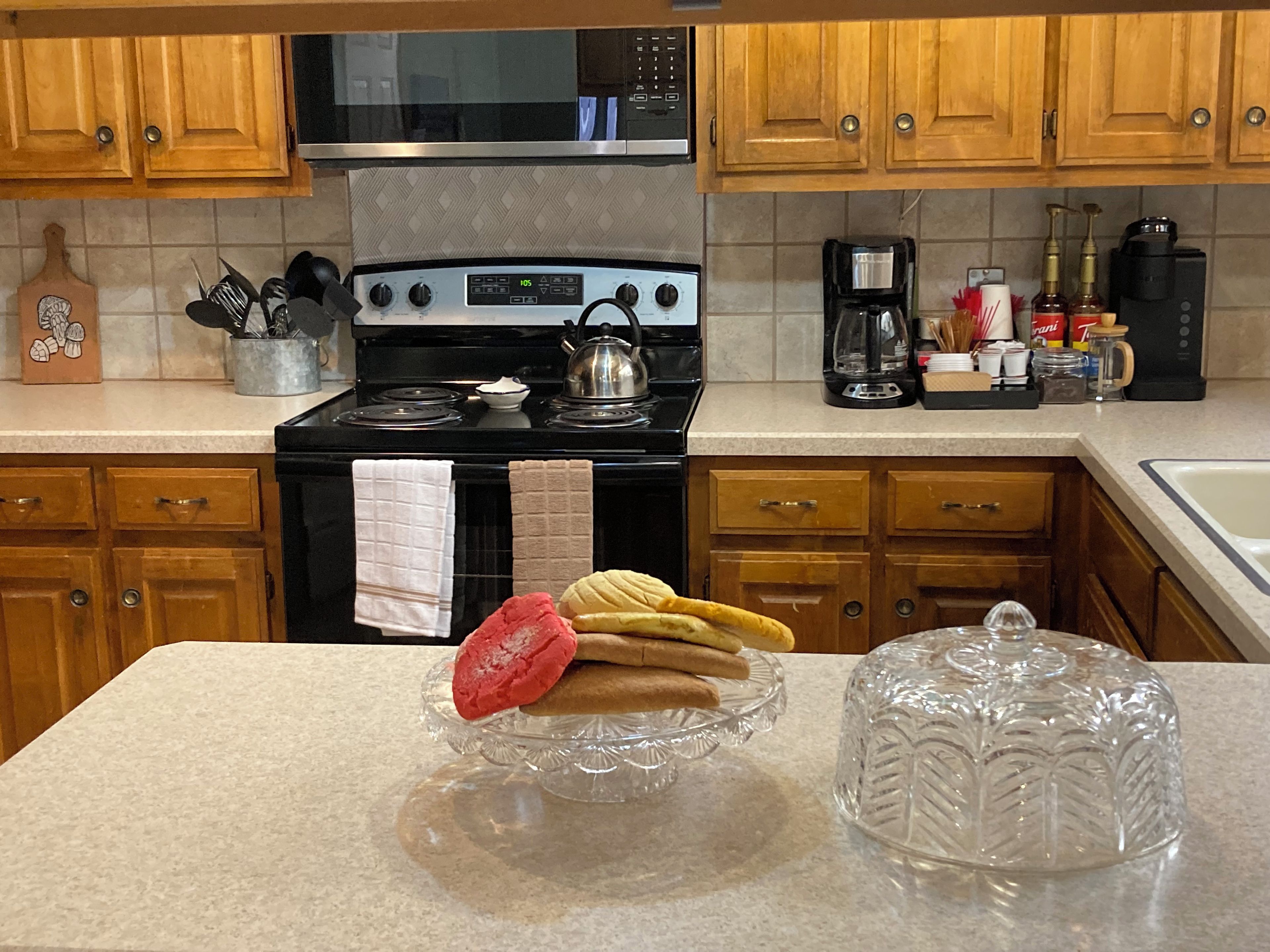 A kitchen with wooden cabinets, a stainless steel stove, and a countertop with a glass cake stand and a clear glass container.