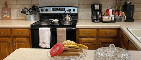 Una cocina con armarios de madera, una estufa de acero inoxidable y una encimera con un expositor de vidrio para pasteles y un recipiente de vidrio transparente.