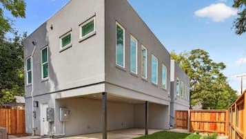 A modern two-story house with a flat roof, a covered patio area, and a fenced backyard.