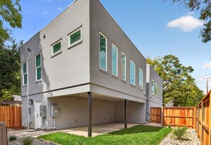 Una casa moderna de dos pisos con techo plano, un patio cubierto y un patio trasero cercado.