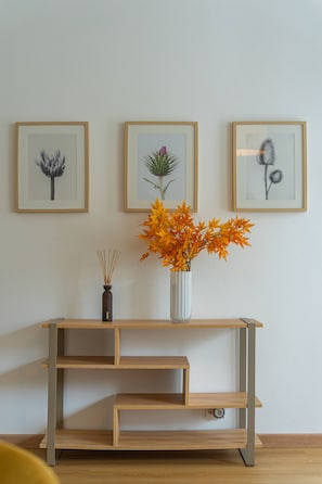A wooden console table with a vase of orange leaves, flanked by three framed botanical illustrations on the wall. - Casa dos Amigos by Galmi (Câmara de Lobos)