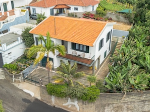 A two-story house with a tiled roof, a balcony, and a garden with various plants. - Casa dos Amigos by Galmi (Câmara de Lobos)