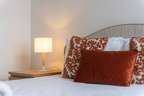 A neatly made bed with white bedding and a brown pillow, a bedside lamp, and a grey headboard. - Casa dos Amigos by Galmi (Câmara de Lobos)