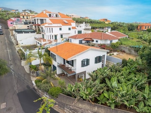A residential area with multiple houses, each featuring a red-tiled roof and white walls, surrounded by lush greenery and a clear sky. - Casa dos Amigos by Galmi (Câmara de Lobos)