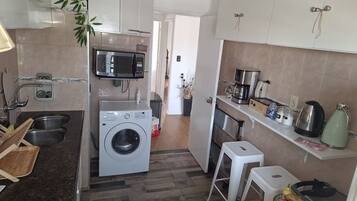 A compact kitchen with a washing machine, microwave, and a coffee maker.