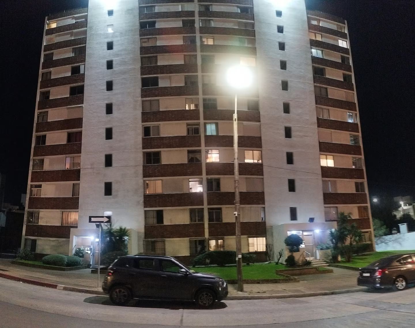 Ein mehrstöckiges Gebäude mit einem zentralen Lichtmast, einem Parkplatz und einem gepflegten Rasen.