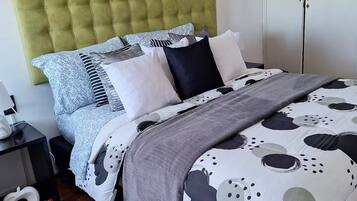 A modern bedroom with a tufted green headboard, a patterned bedspread, and a wooden parquet floor.