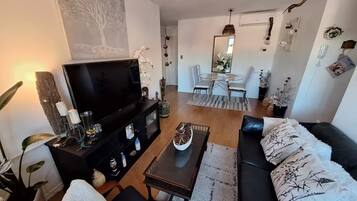 A living room with a TV, sofa, coffee table, and a dining area with chairs and a table.