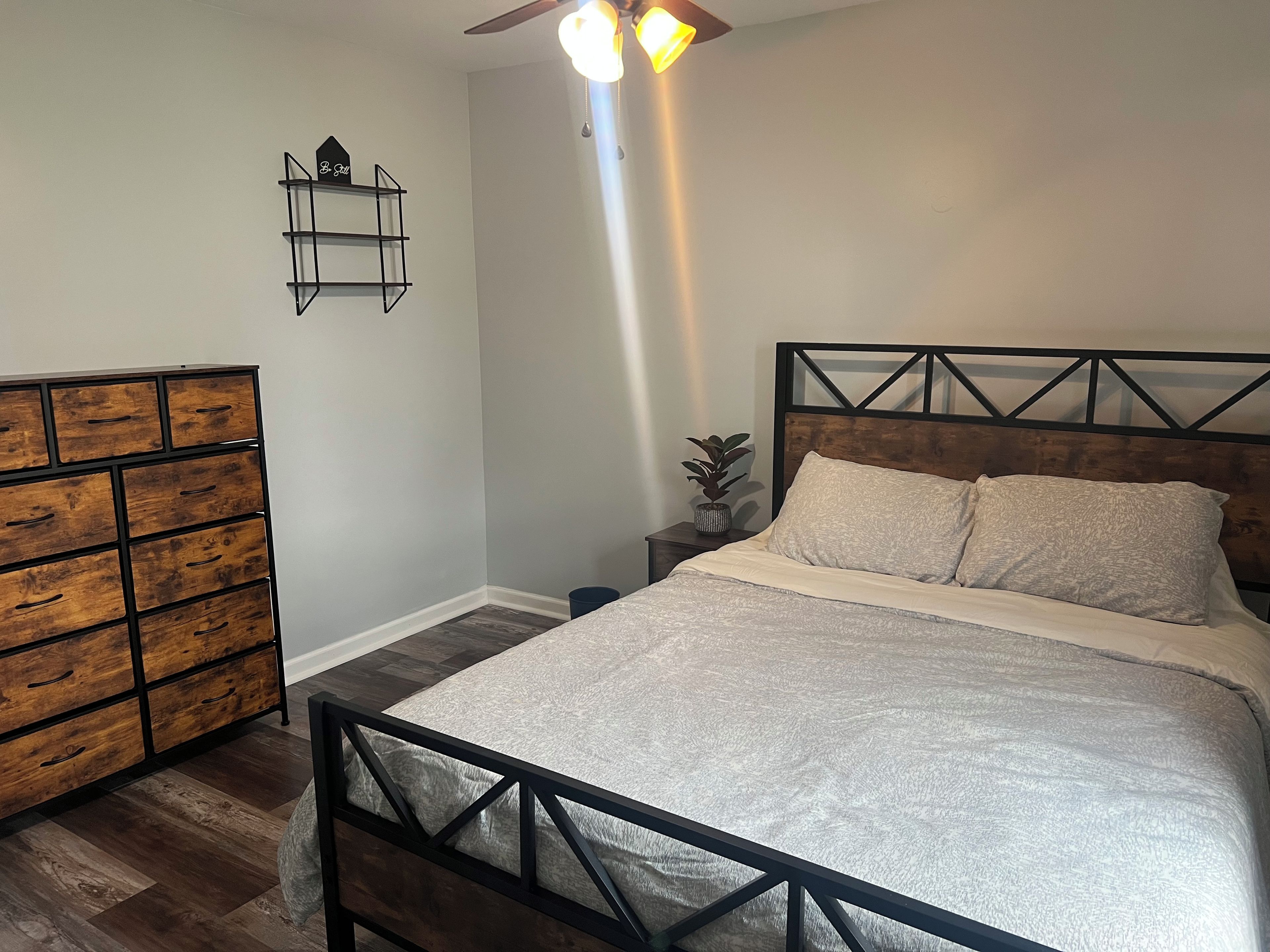 Un dormitorio con cama, cómoda, mesita de noche y ventilador de techo.