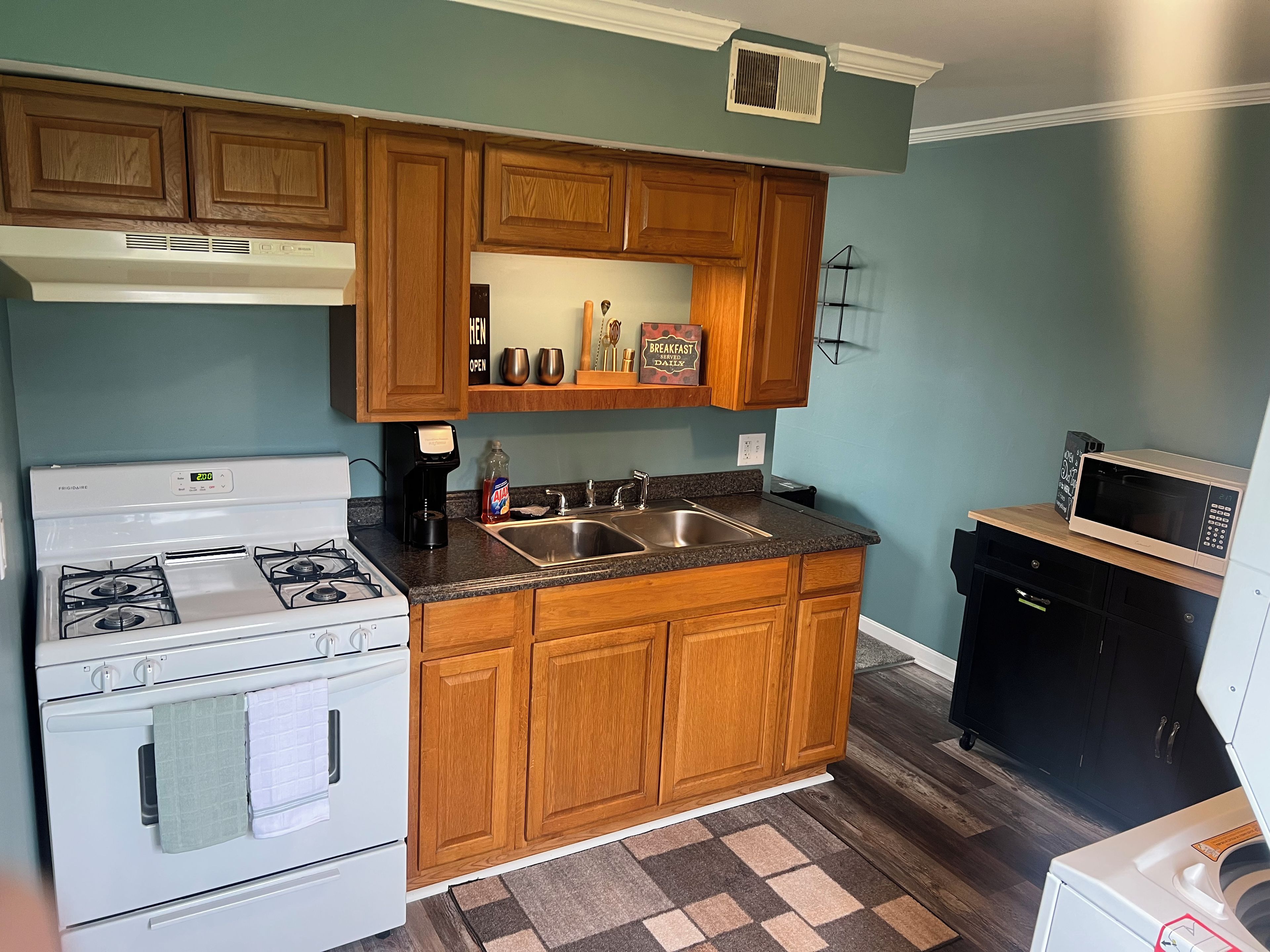 A kitchen with wooden cabinets, a white stove, a sink, and a microwave.