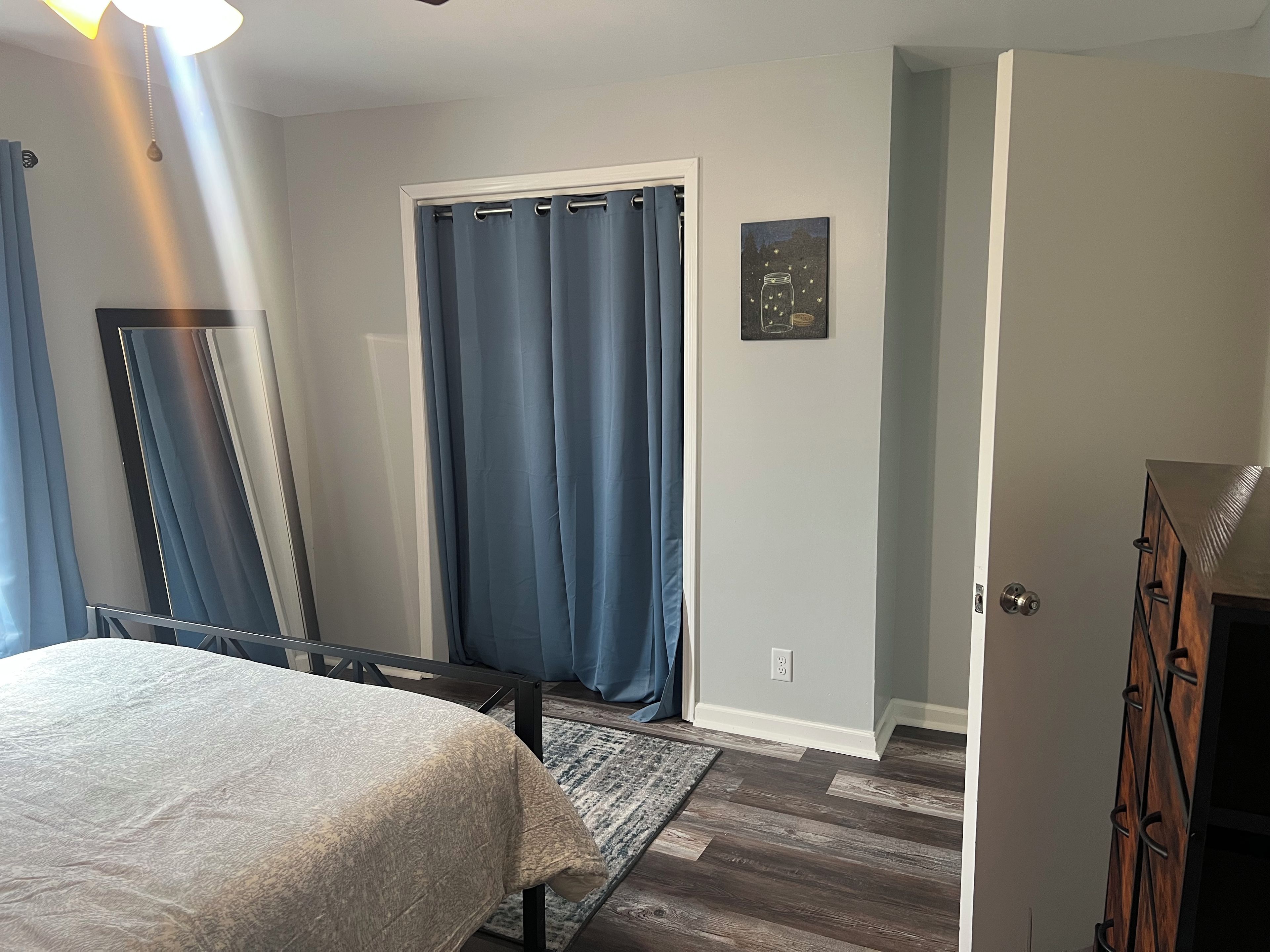 Un dormitorio con una cama, una puerta, un espejo y un cuadro colgado en la pared.