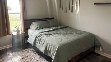 Un dormitorio con cama, ventilador de techo, ventana con cortinas y espejo montado en la pared.