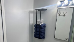 A bathroom with a toilet, sink, towel rack, and a mirror with lights.