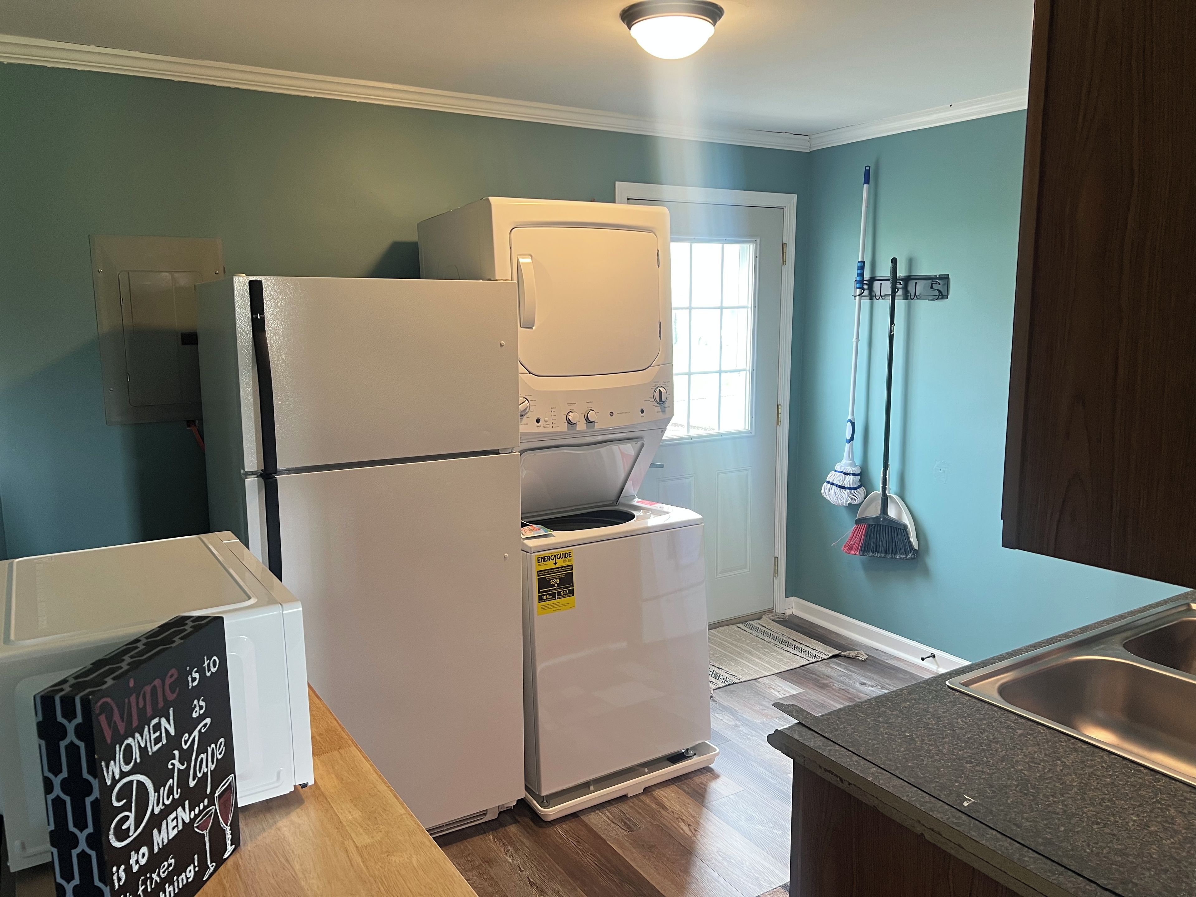 Una cocina compacta con refrigerador, horno y microondas. Hay un cartel en el refrigerador, una encimera de madera y una ventana con vistas.