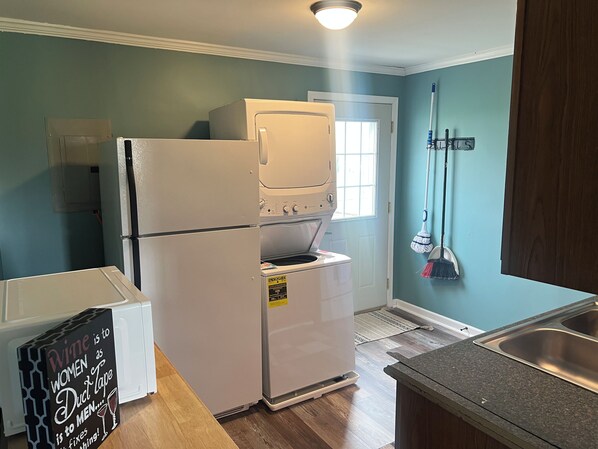 A compact kitchen with a refrigerator, oven, and microwave. There's a sign on the fridge, a wooden countertop, and a window with a view.