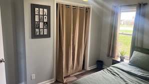 A bedroom with a bed, a ceiling fan, a window with curtains, a wall-mounted picture frame, and a small plant.