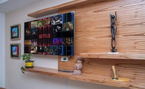 A wall-mounted TV with a Netflix logo, a wooden shelf with a small figurine, and a potted plant. - Modern 2BR | Indoor Pool, Balcony & Free Parking (Asunción)