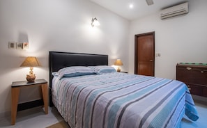 A bedroom with a bed, two bedside tables with lamps, a wall-mounted light fixture, a wooden door, and an air conditioning unit. - Modern 2BR | Indoor Pool, Balcony & Free Parking (Asunción)