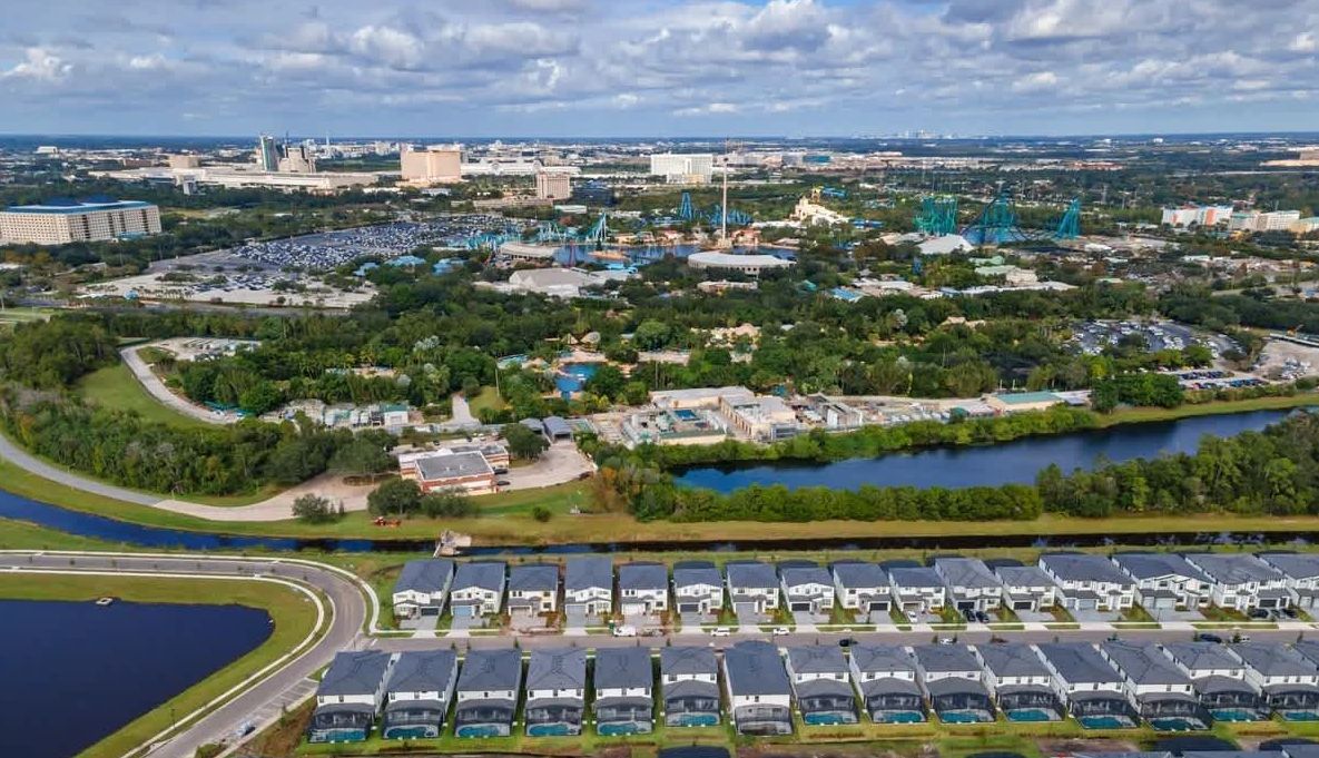 Vista aerea di una zona residenziale con diverse case, un parcheggio e un corpo d'acqua.