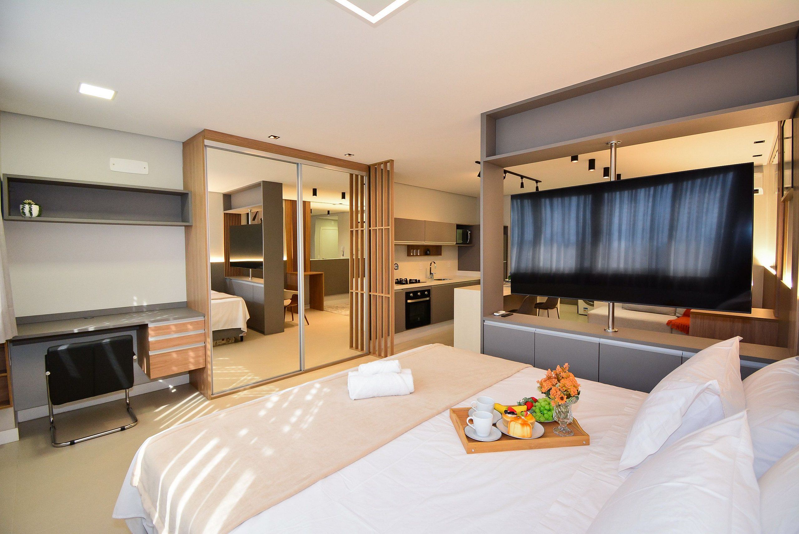 Une chambre d’hôtel équipée d’un lit, d’un bureau, d’une télévision, d’un miroir et d’une kitchenette.