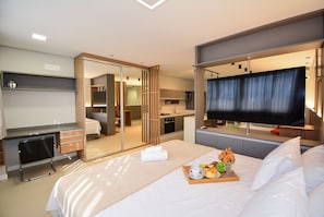 Ein Hotelzimmer mit Bett, Schreibtisch, Fernseher, Spiegel und einer Küchenzeile.