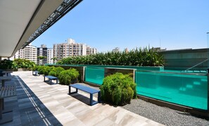 A rooftop terrace with a swimming pool, seating areas, and a view of surrounding buildings. - Studio Jardim Milano - CEN015 (Florianópolis)