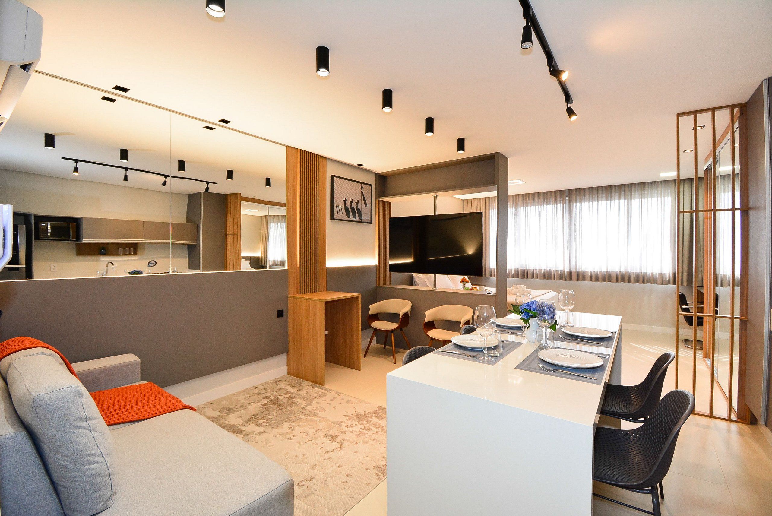 Een moderne woonkamer met een bank, een eethoek met een tafel gedekt voor twee personen, en een keuken op de achtergrond.