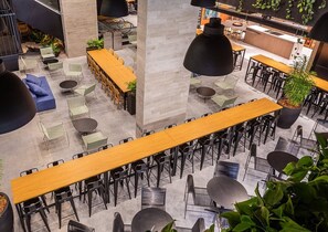 A modern indoor space with multiple seating areas, including tables and chairs, and a central column. - Studio Jardim Milano - CEN015 (Florianópolis)