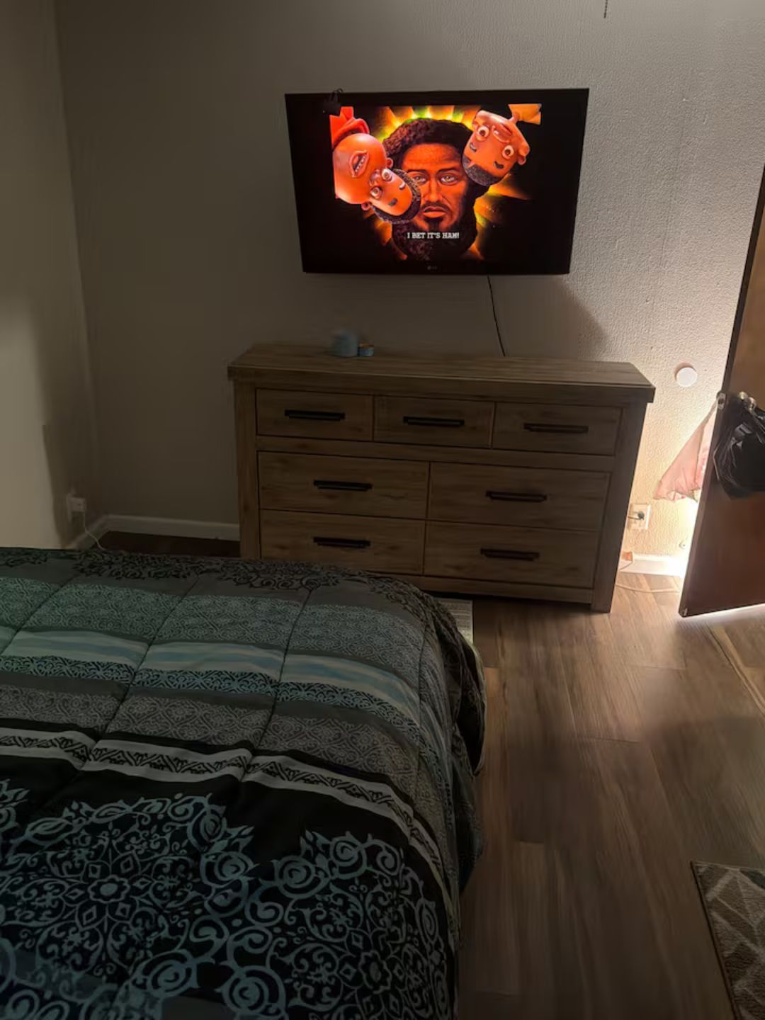 A bedroom with a bed, a wooden dresser, and a television mounted on the wall.