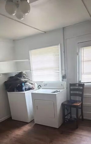 A laundry room with a washing machine and dryer, a chair, and a window with blinds. - Cozy modern ranch retreat 2BR & 1BA (St. Louis)