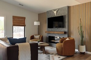 A modern living room with a flat-screen TV, a fireplace, and a large window with blinds. - Red Rock Views, Rooftop Patio, Hot Tub, Updated (Sedona)