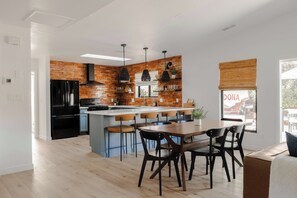 A modern kitchen with a brick backsplash, black appliances, and a central island with bar stools. - Red Rock Views, Rooftop Patio, Hot Tub, Updated (Sedona)
