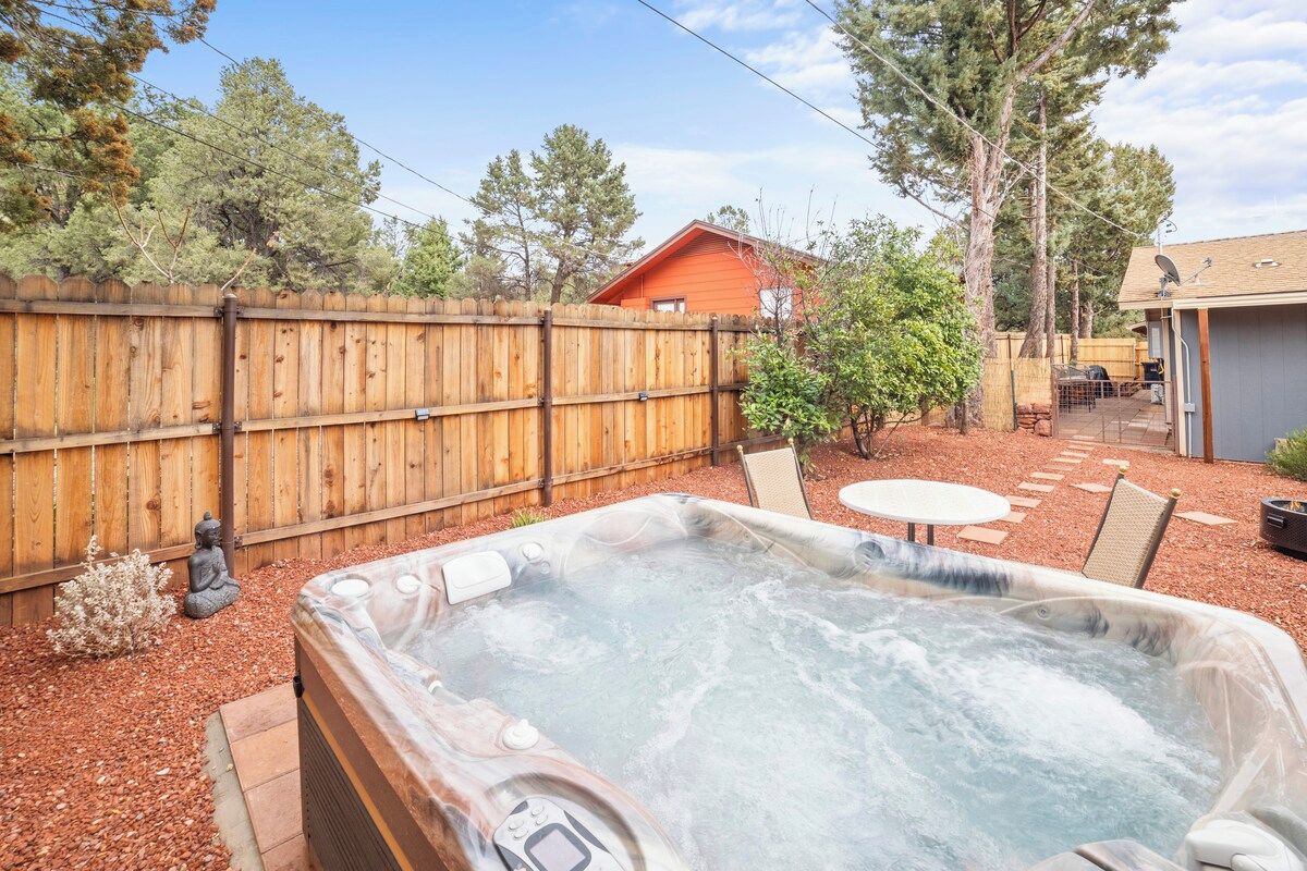 A hot tub in a backyard with a wooden fence, a small garden, and a house in the background.