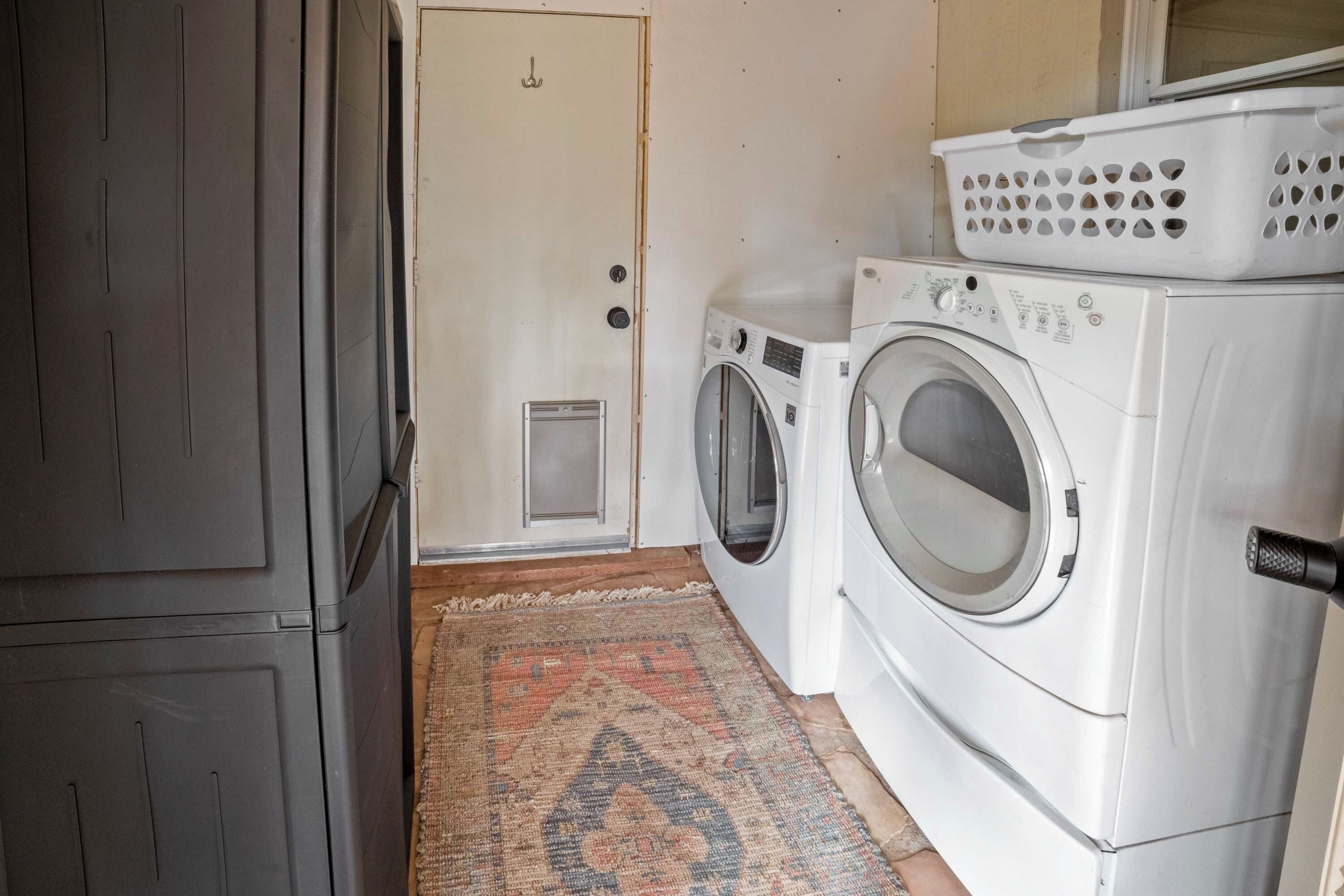 A laundry room with two front-loading washing machines, a drying rack, and a door.